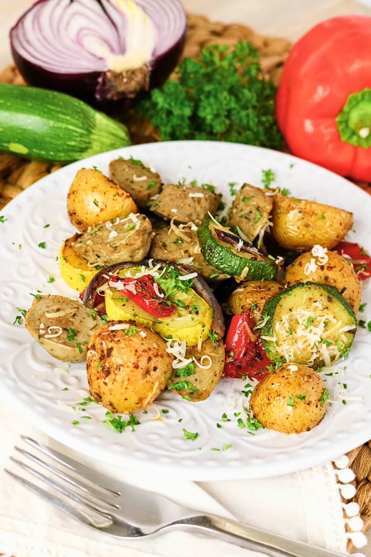 Roasted potatoes, sausage, and vegetables on a white plate with shredded cheese.