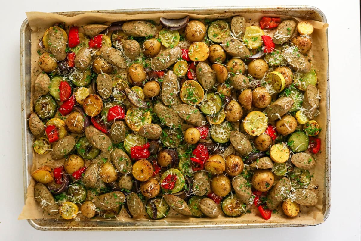Roasted sausages, potatoes, and vegetables on a parchment-lined baking sheet.