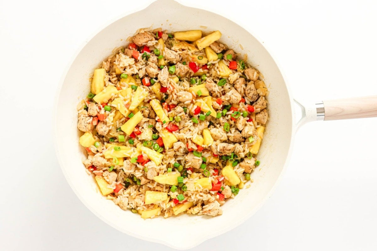 Stir-fry with chicken, pineapple, rice, and colorful vegetables in a white pan.