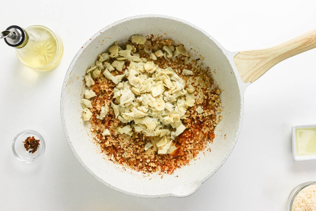 White skillet with chopped artichokes, and spices on a white background.