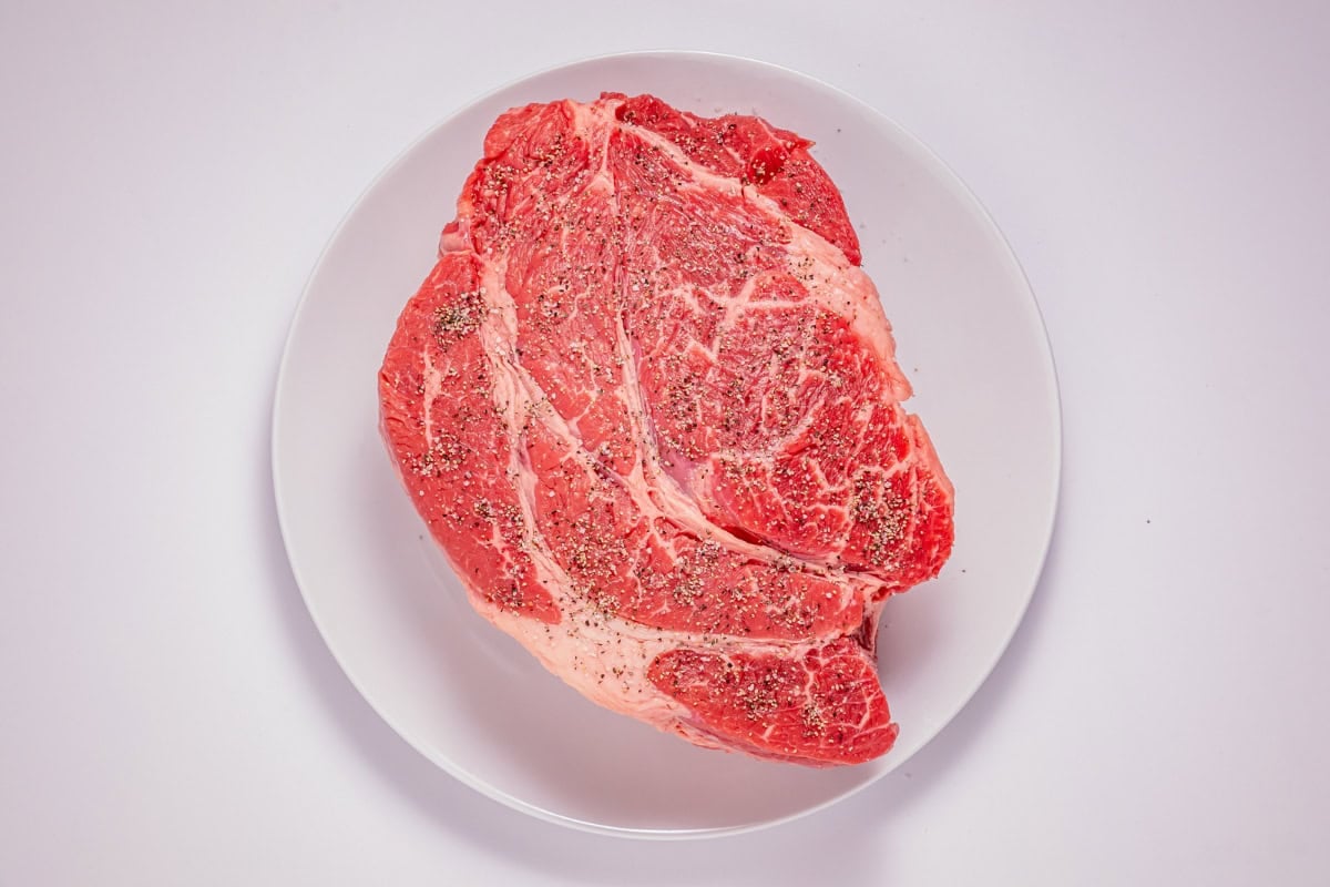 Raw seasoned steak on a white plate, viewed from above.