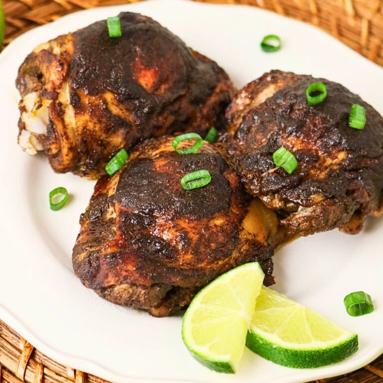 Three pieces of jerk chicken garnished with green onions, served with lime wedges.