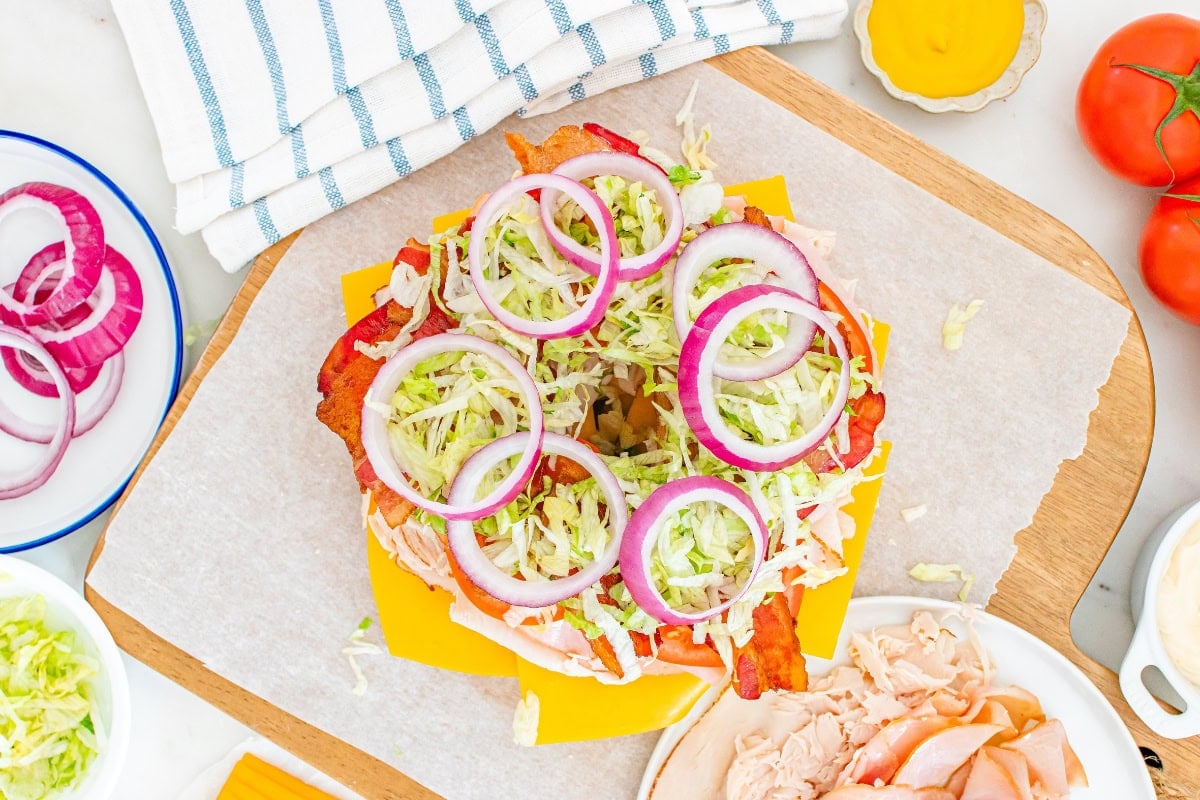 Open-faced sandwich with cheese, bacon, lettuce, and red onion rings.