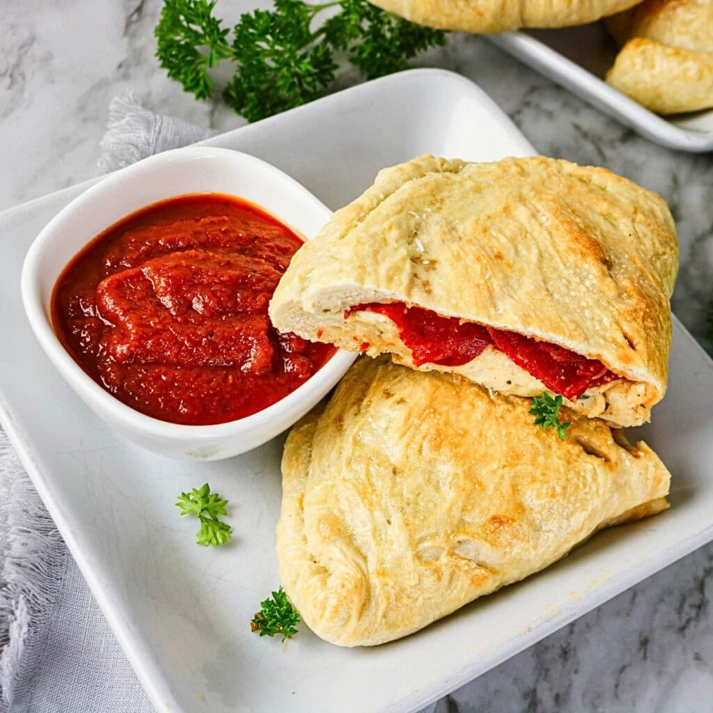 Golden calzones with red sauce in a small bowl, garnished with parsley.
