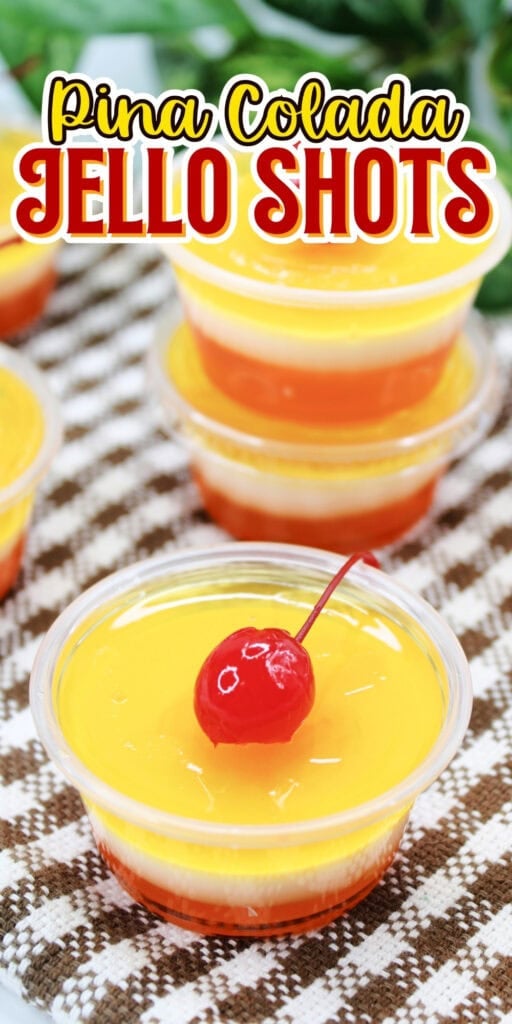 Plastic cups with yellow-orange jello topped with cherries on a checkered cloth.