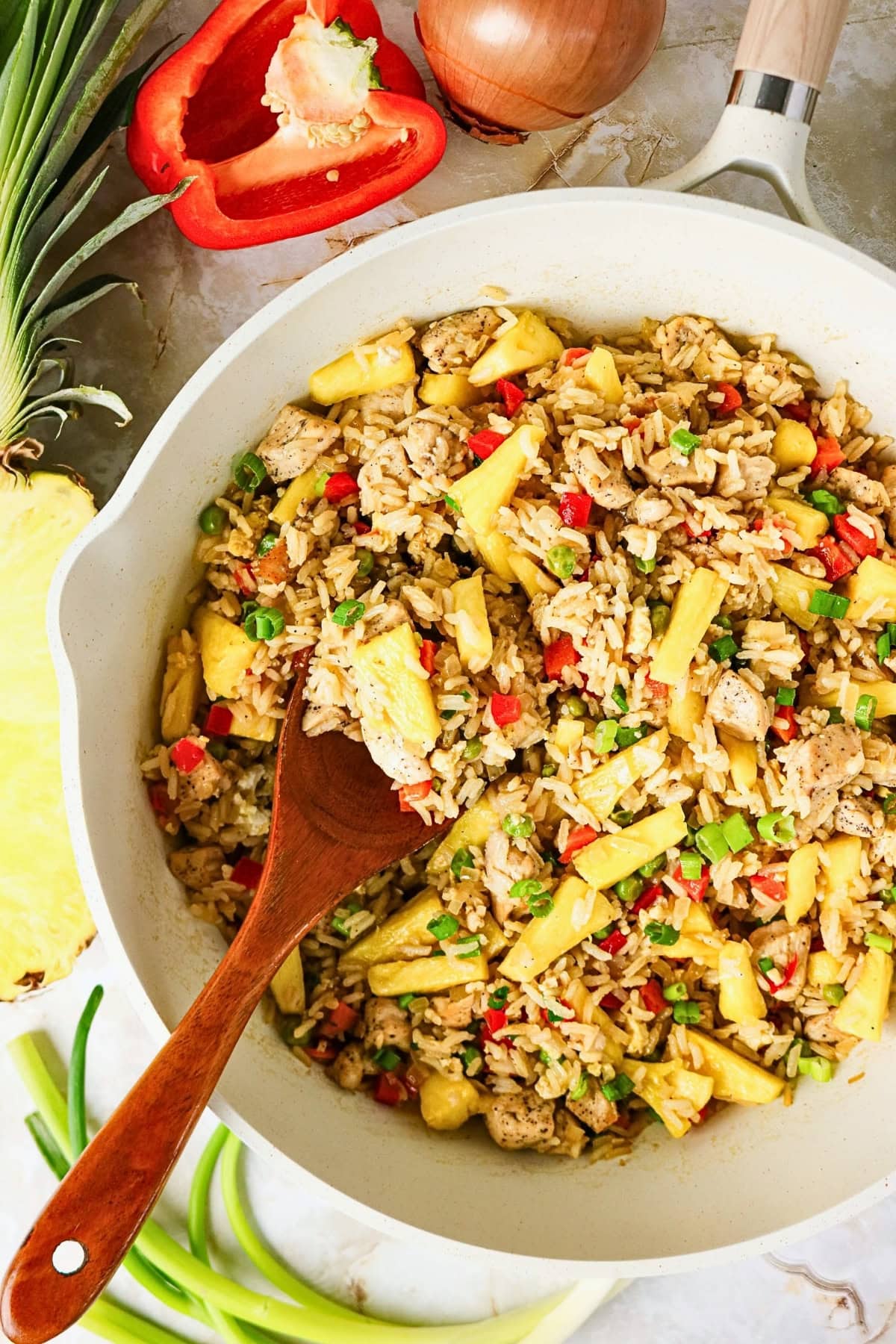 Fried rice with chicken, pineapple, and vegetables in a white skillet.