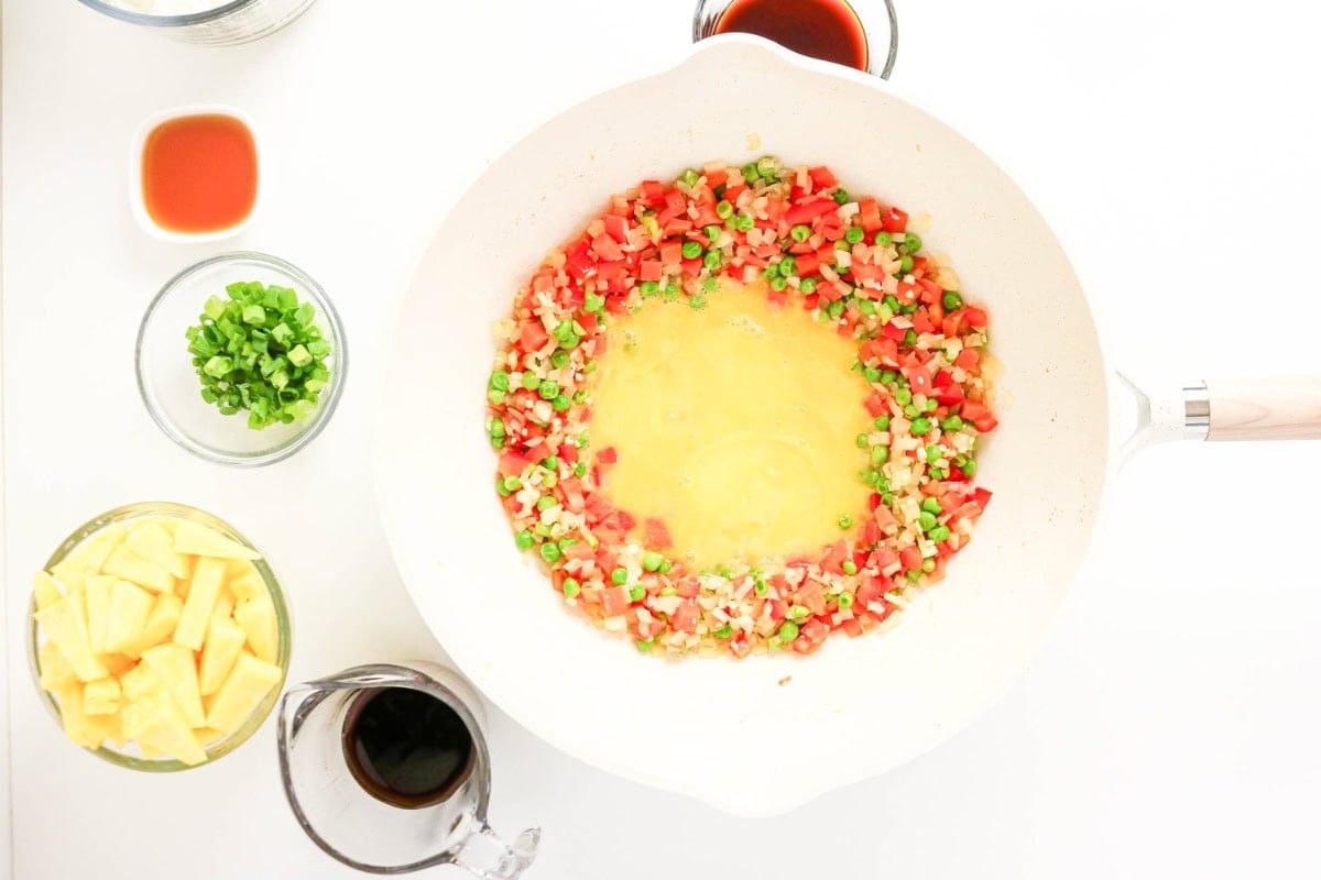 Veggies cook in a pan, egg in the center, with pineapple waiting nearby.