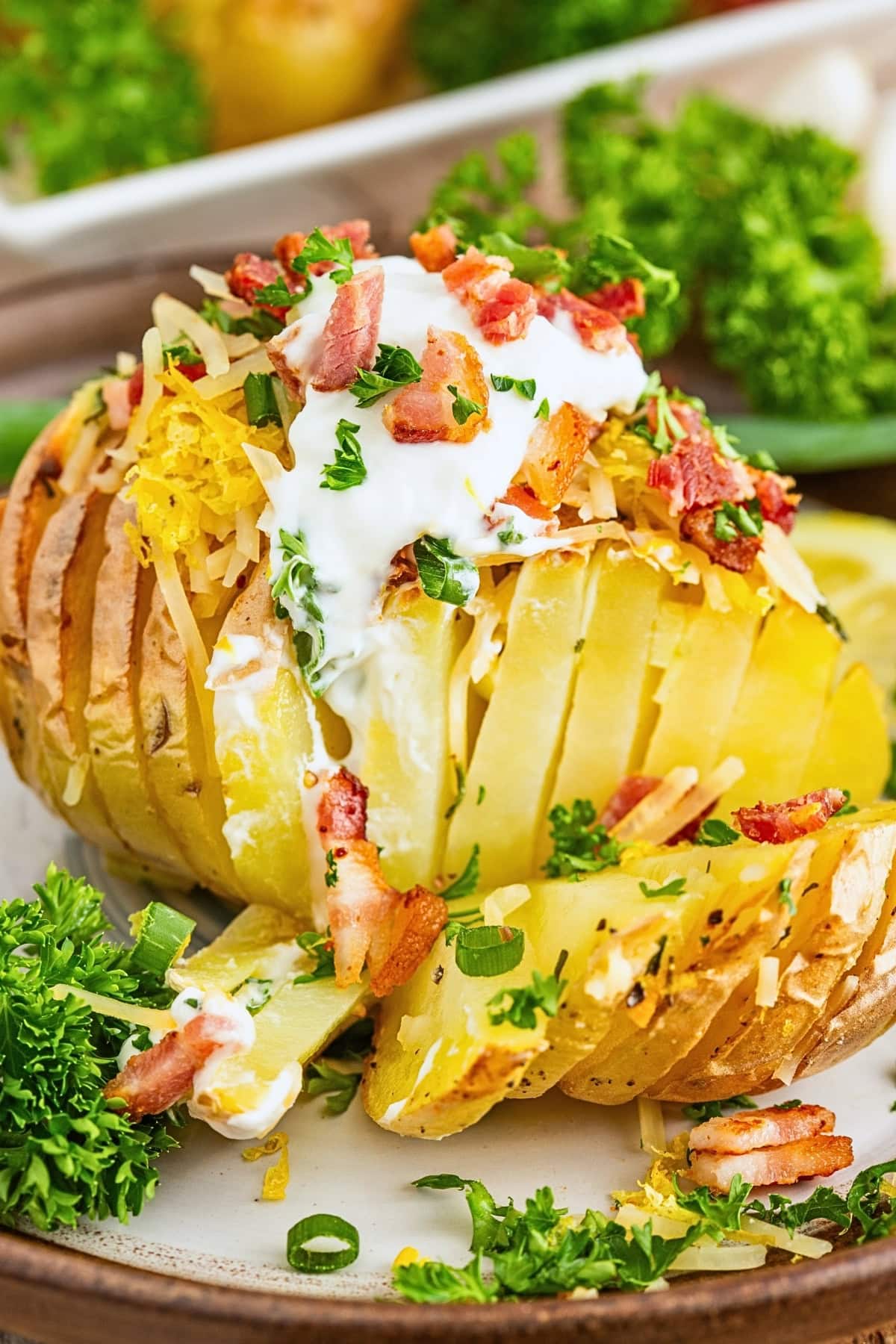 Sliced baked potato with sour cream, cheese, bacon, and herbs on a plate.