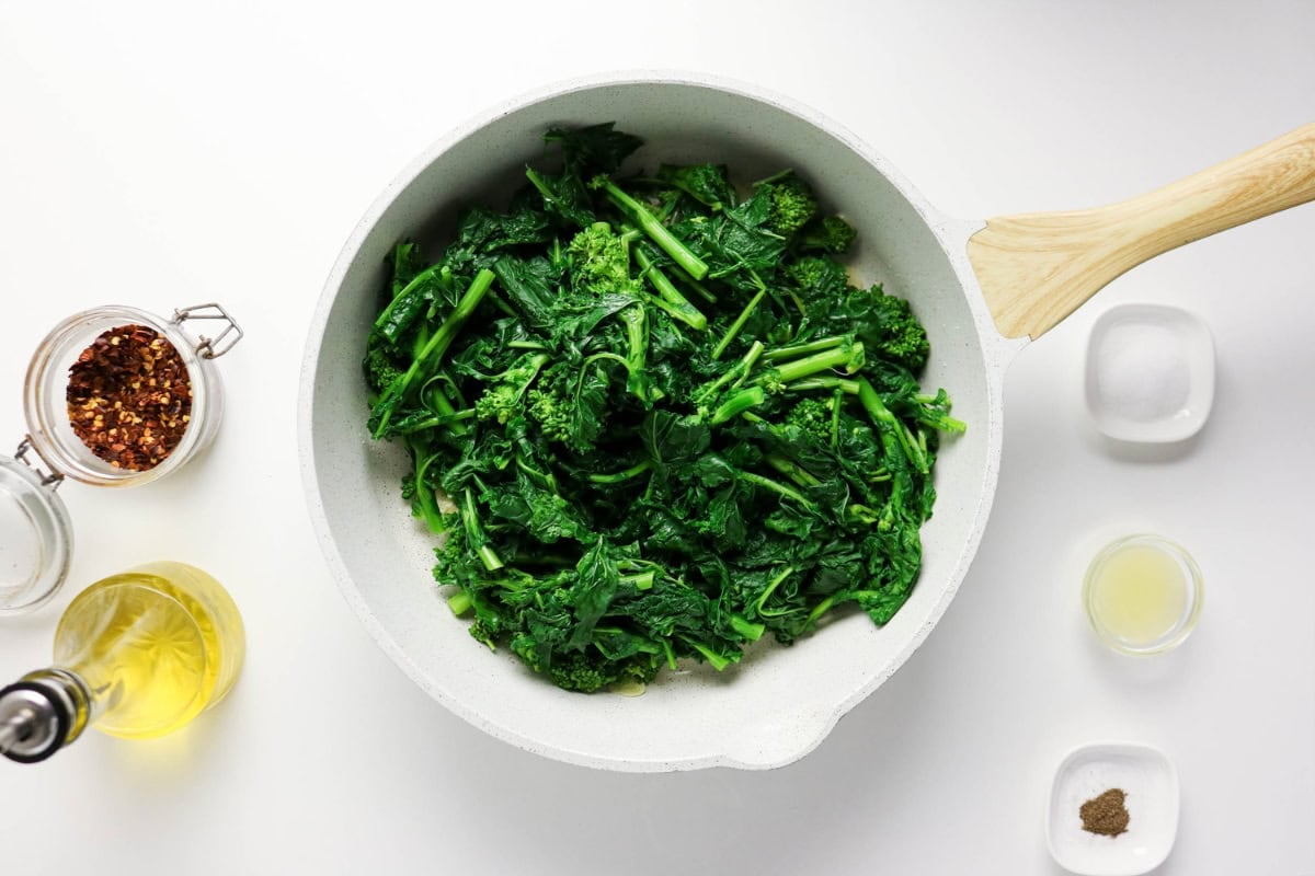 Cooked leafy greens in a white pan with seasonings and oil nearby.