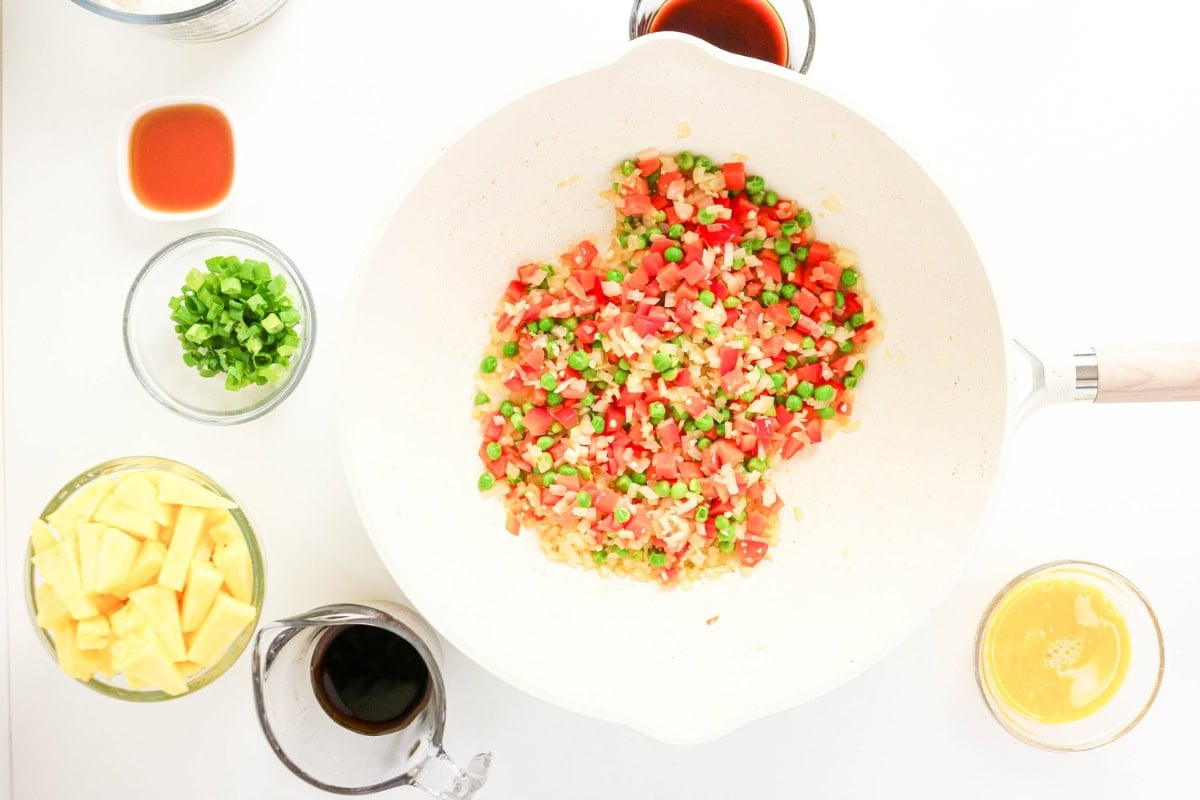 Diced vegetables cooking in a white pan, surrounded by bowls of ingredients.