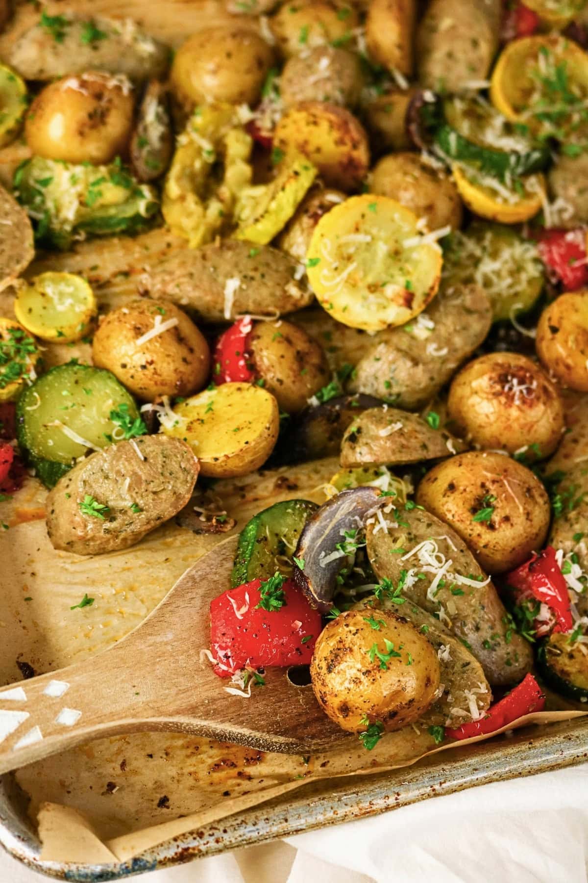 Roasted potatoes, sausage, and vegetables on a baking sheet with herbs.