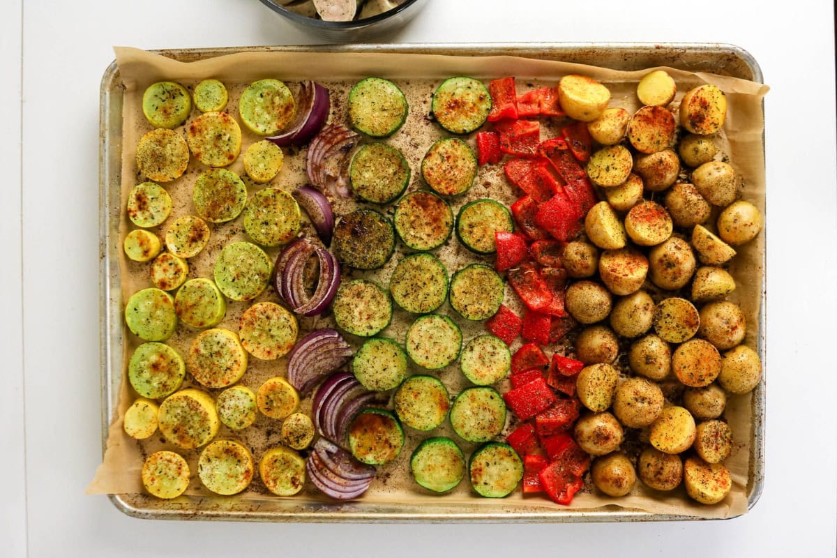 Sliced vegetables and potatoes seasoned on a baking sheet lined with parchment.