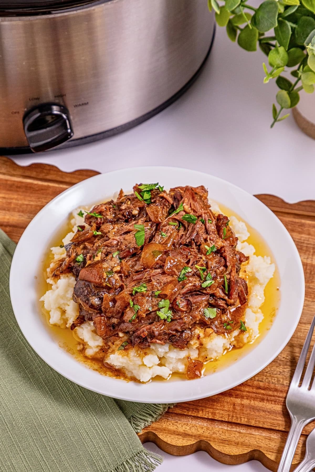 Shredded beef with gravy on mashed potatoes, garnished with parsley.