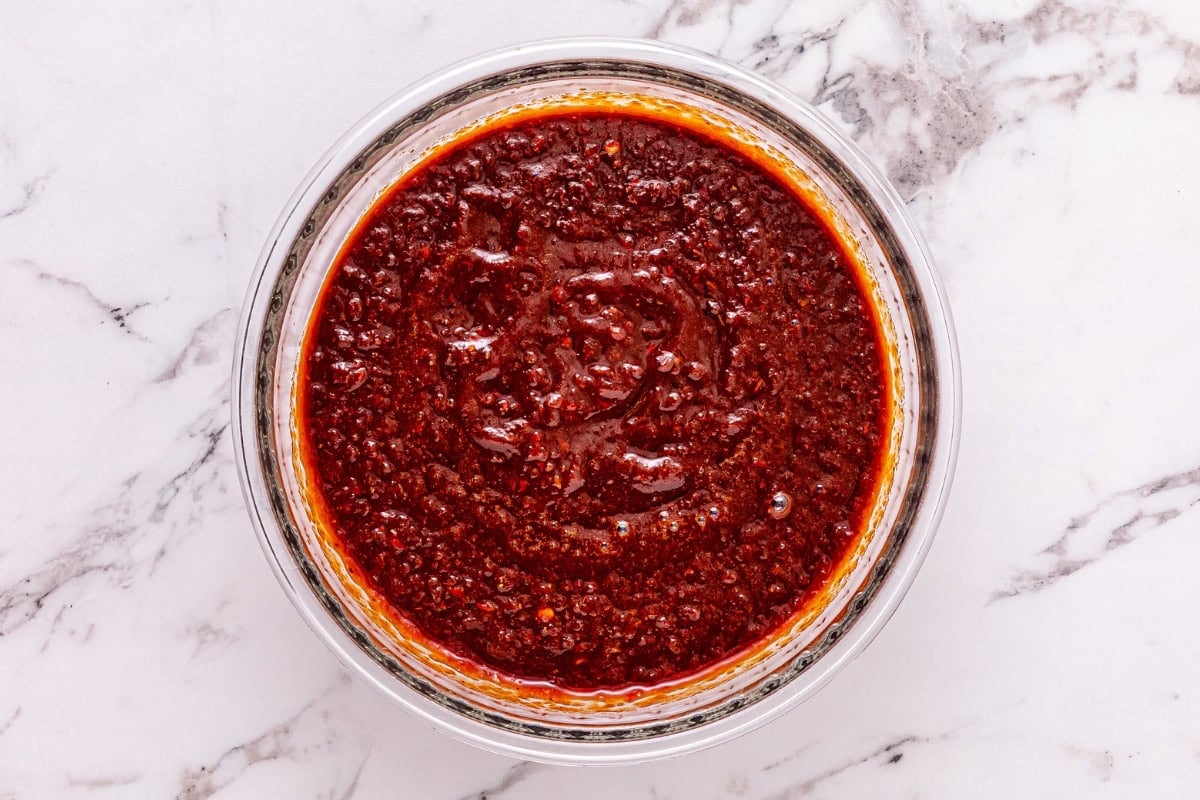 A bowl of red chili sauce on a white marble surface.