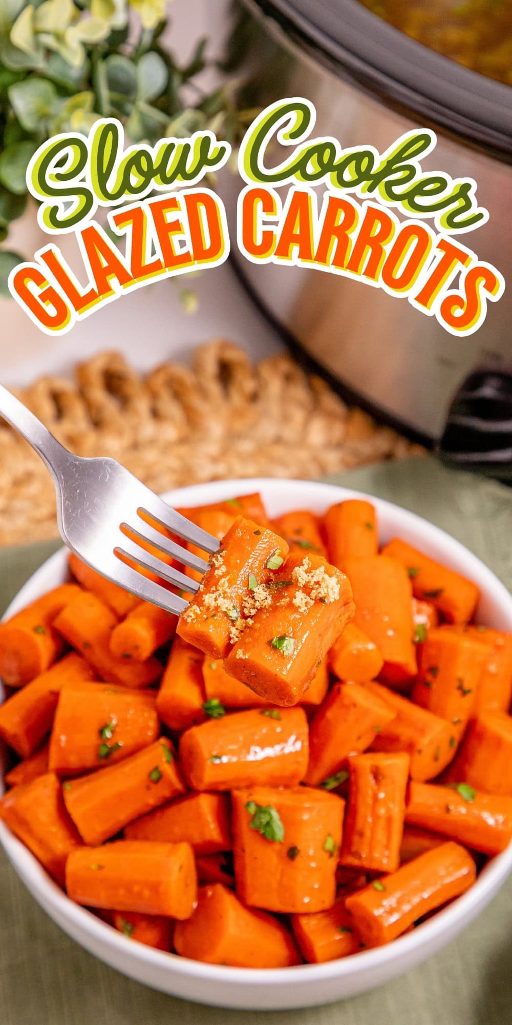 Fork holding glazed carrot above bowl, slow cooker in background.