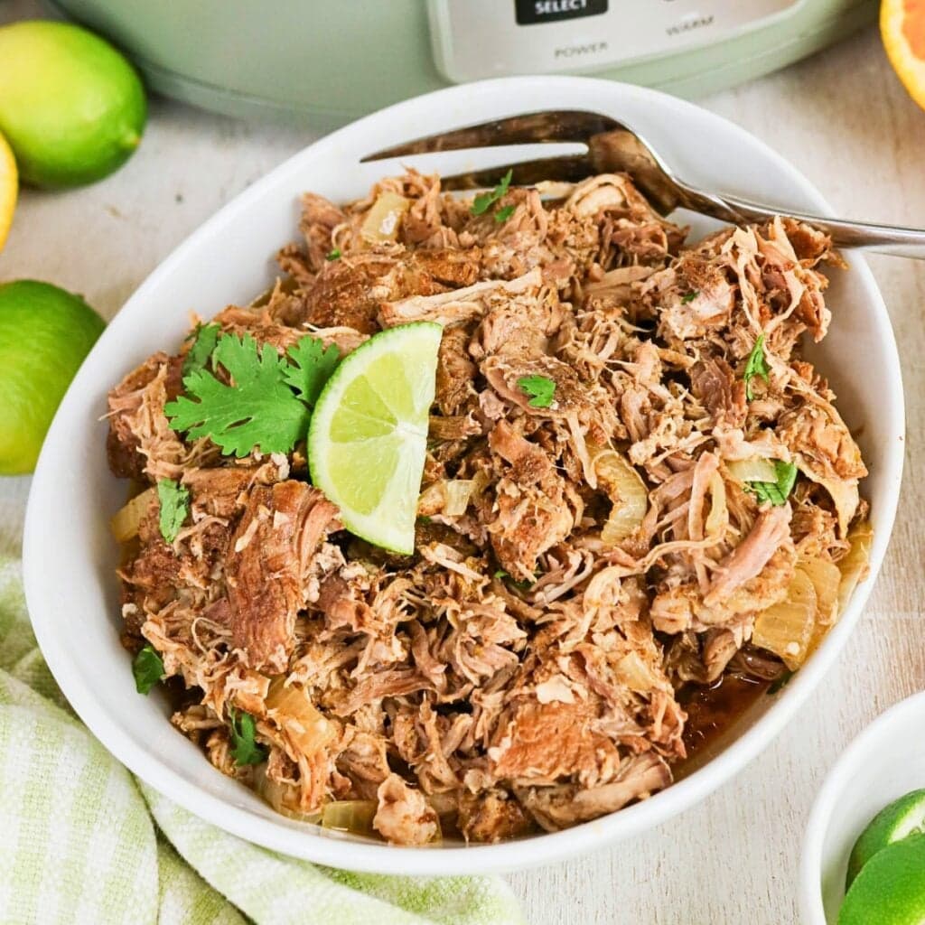 Shredded pork in a bowl, garnished with cilantro and a lime wedge.