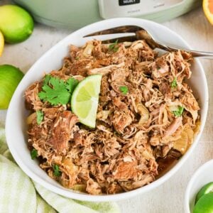 Shredded pork in a bowl, garnished with cilantro and a lime wedge.