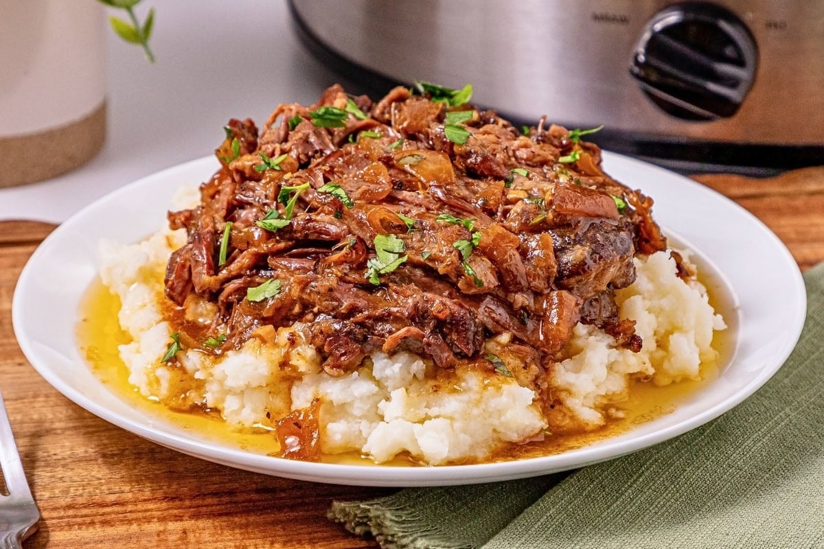 Shredded beef with gravy over mashed potatoes, garnished with parsley.
