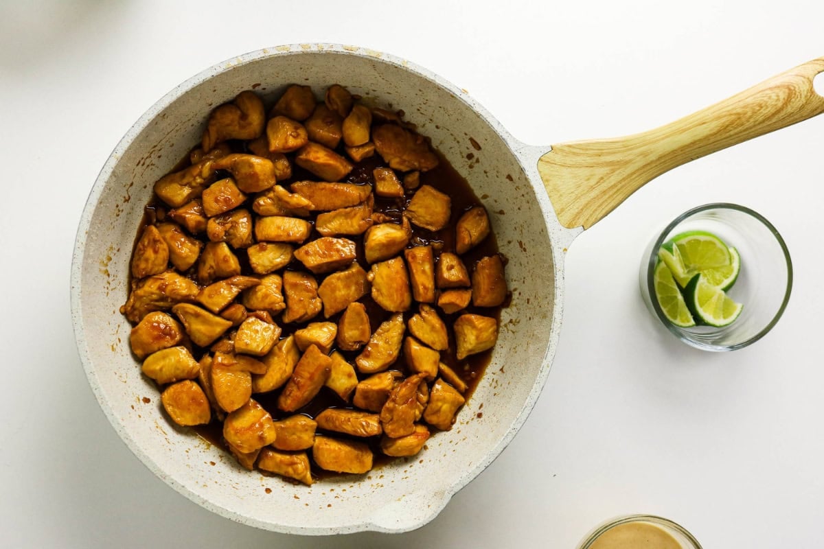 A pan of cooked, saucy chicken pieces beside a glass with lime wedges.