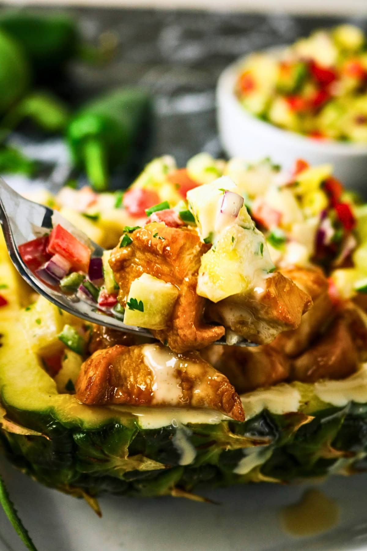 A fork lifts saucy chicken and pineapple salsa from a hollowed pineapple bowl.