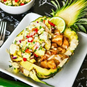 Chicken and vegetables served in a pineapple bowl, topped with creamy sauce.