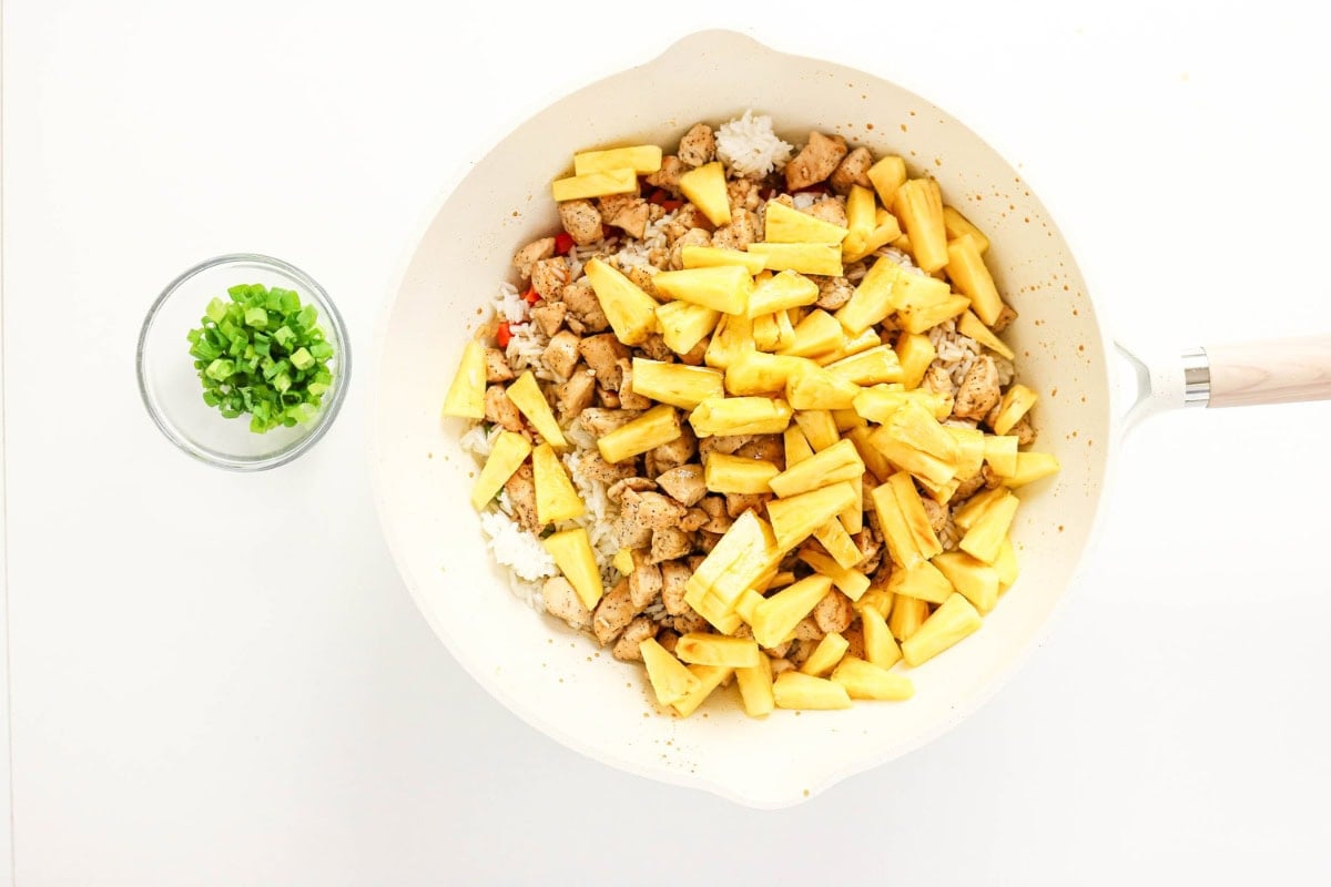 Chicken, pineapple, rice, and vegetables in a skillet; green onions in a bowl.