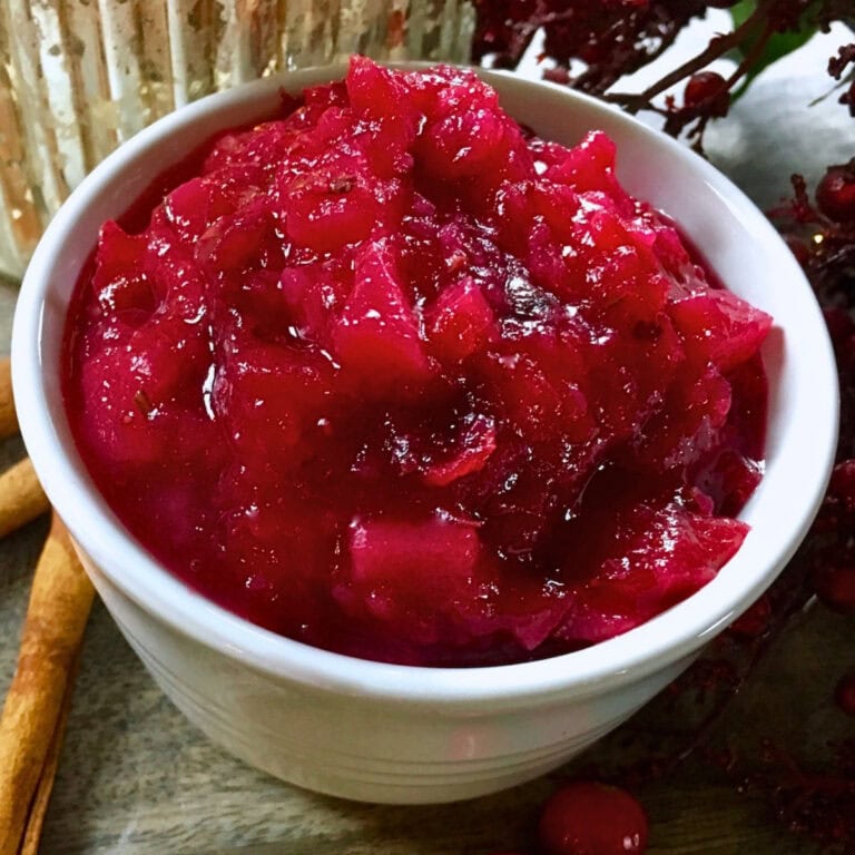 White bowl filled with chunky red cranberry sauce on a wooden surface.