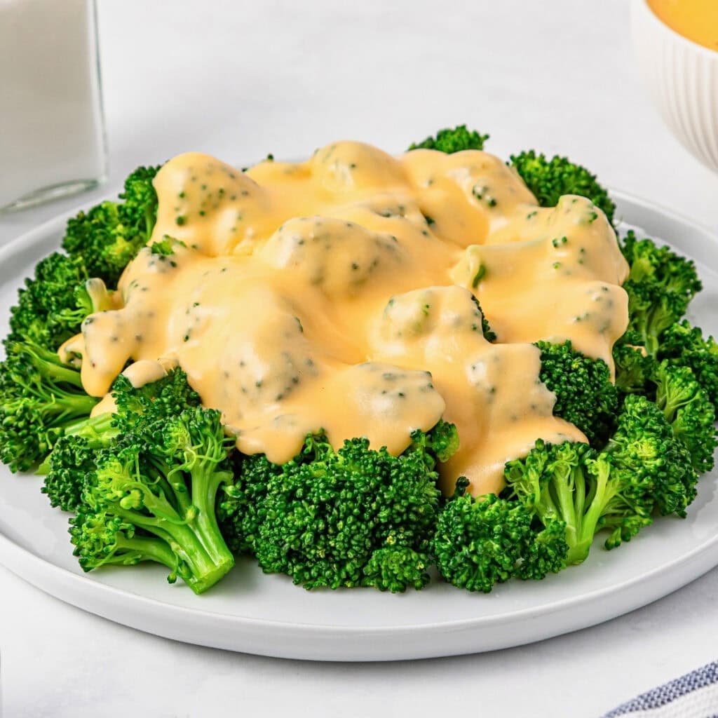 Broccoli florets topped with creamy cheese sauce on a white plate.