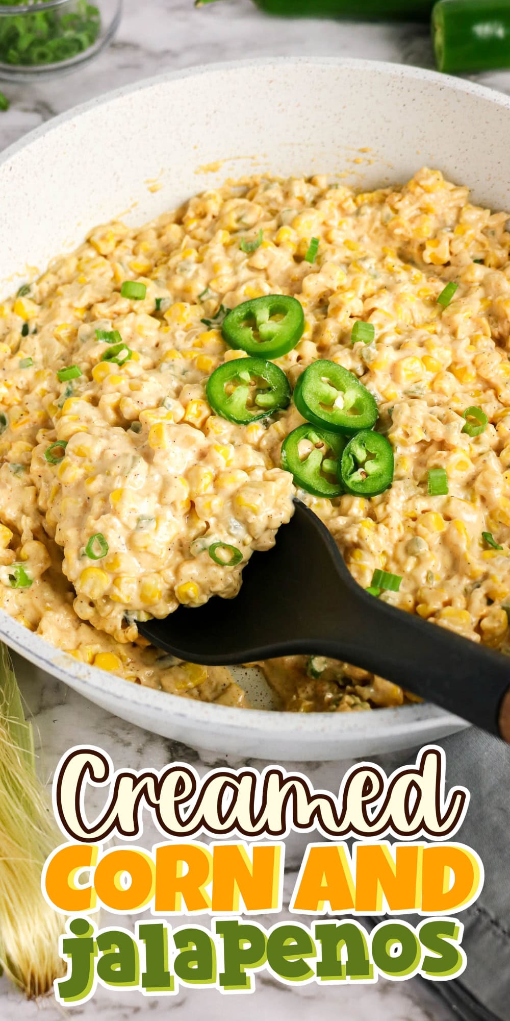 Creamed corn in a skillet, topped with sliced jalapenos and green onions.