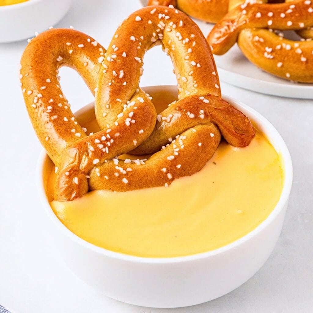 A salted pretzel dipped in a bowl of yellow cheese sauce.