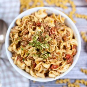 Bowl of pasta with ground meat, tomato sauce, and herbs on top.