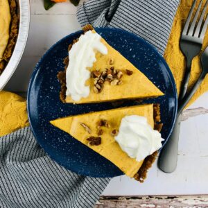 Two pumpkin pie slices with whipped cream and nuts on a blue plate.