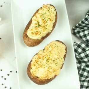 Two twice-baked potatoes topped with cheese and herbs on a white plate.