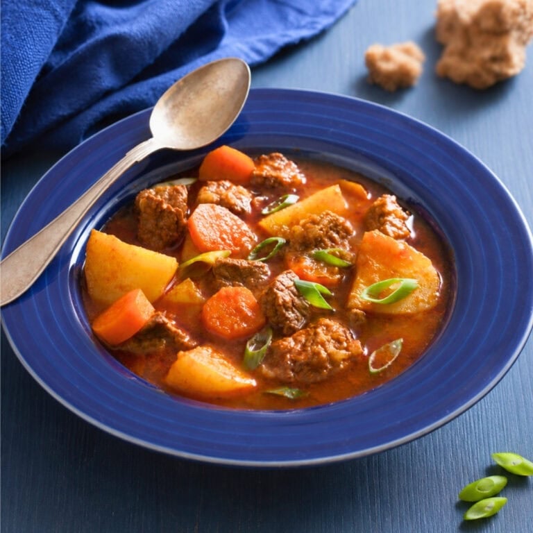 Beef stew with carrots and potatoes in a blue bowl, garnished with green onions.