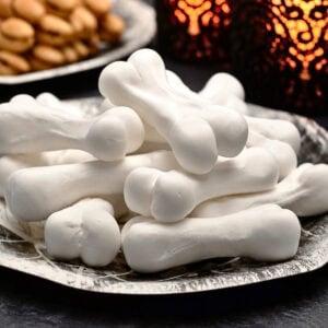 White bone-shaped meringue cookies stacked on a decorative silver plate.