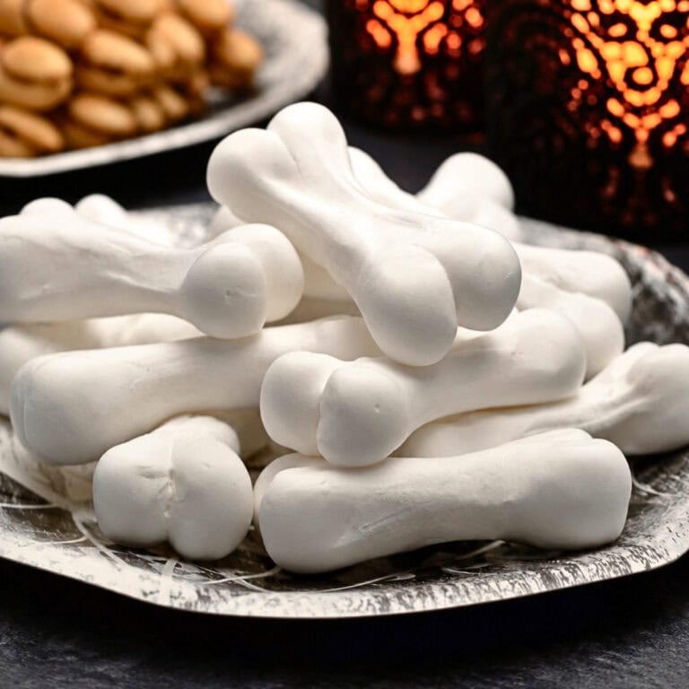 White bone-shaped meringue cookies stacked on a decorative silver plate.