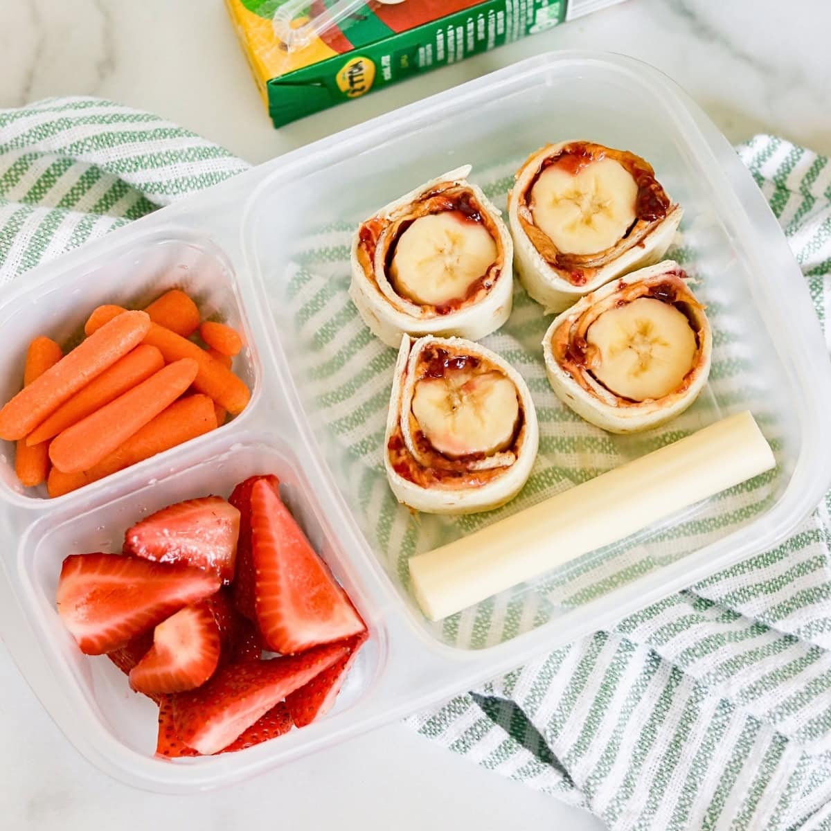 Lunchbox with carrots, strawberries, string cheese, and banana roll-ups.