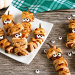 Jalapeno poppers wrapped as mummies with candy eyes on a plate.