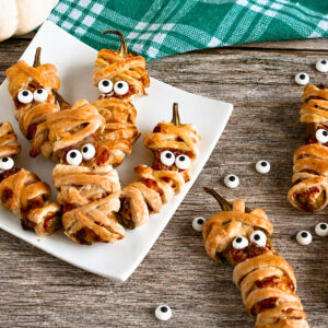 Jalapeno poppers wrapped as mummies with candy eyes on a plate.