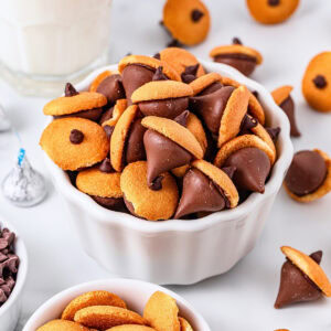 A bowl of chocolate and cookie acorn treats sits on a white surface.