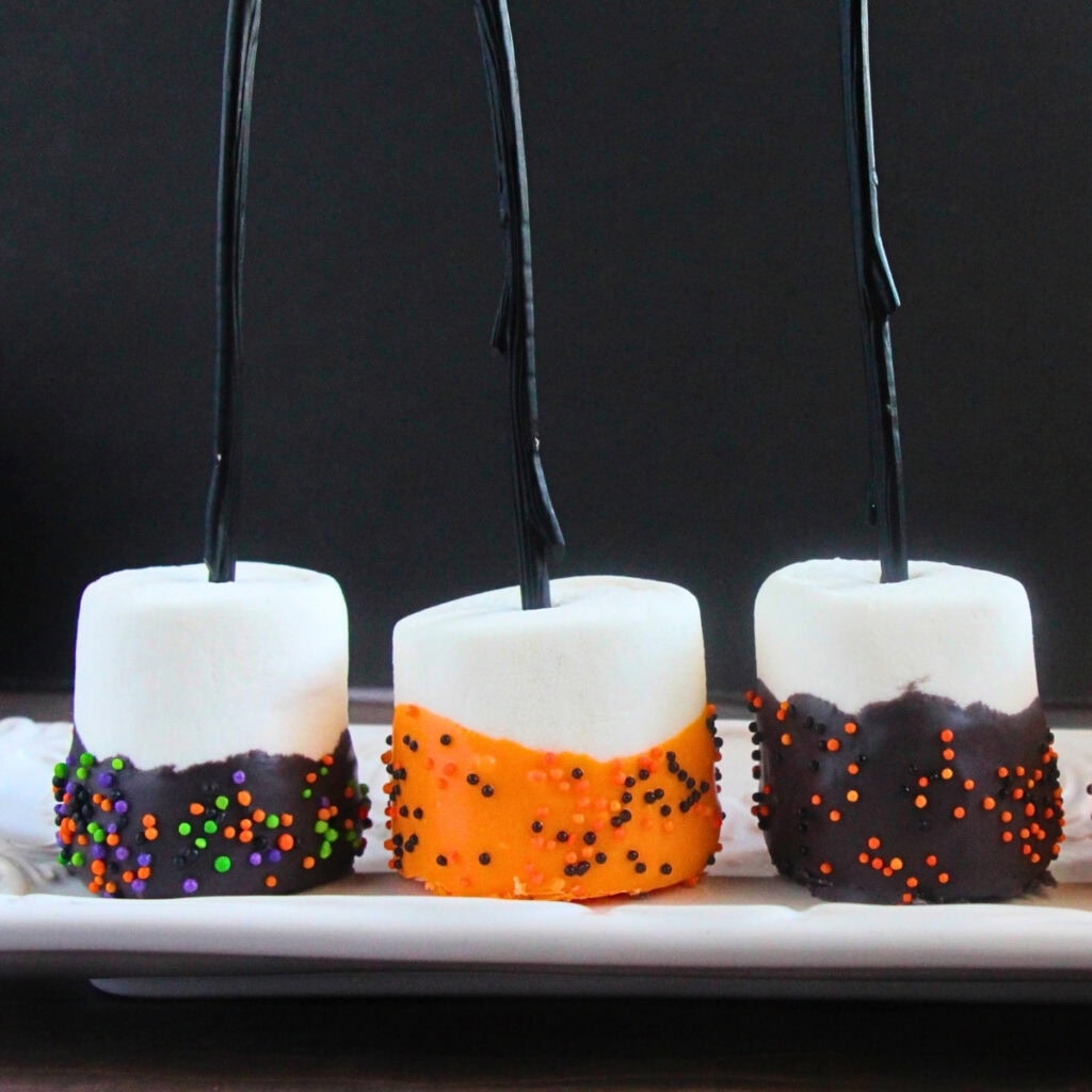 Three marshmallows on sticks dipped in chocolate and orange sprinkles.