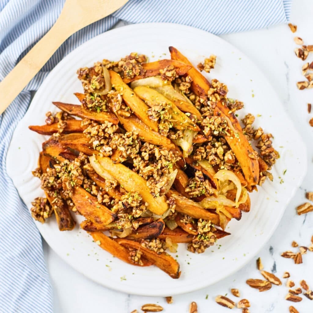 Plate of fries topped with a crunchy nut and seed mixture on a white plate.