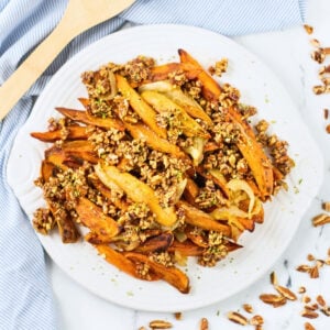 Plate of fries topped with a crunchy nut and seed mixture on a white plate.