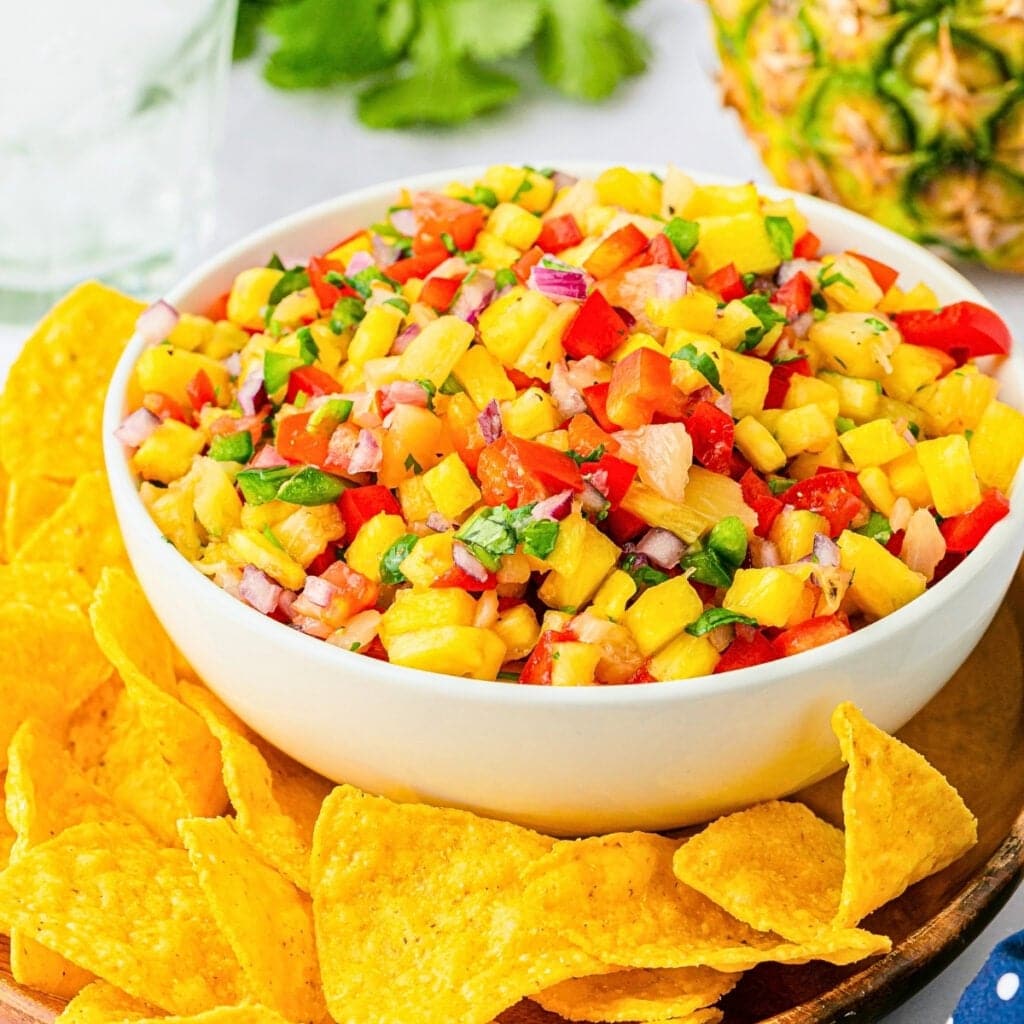 Bowl of pineapple salsa with tortilla chips around it.