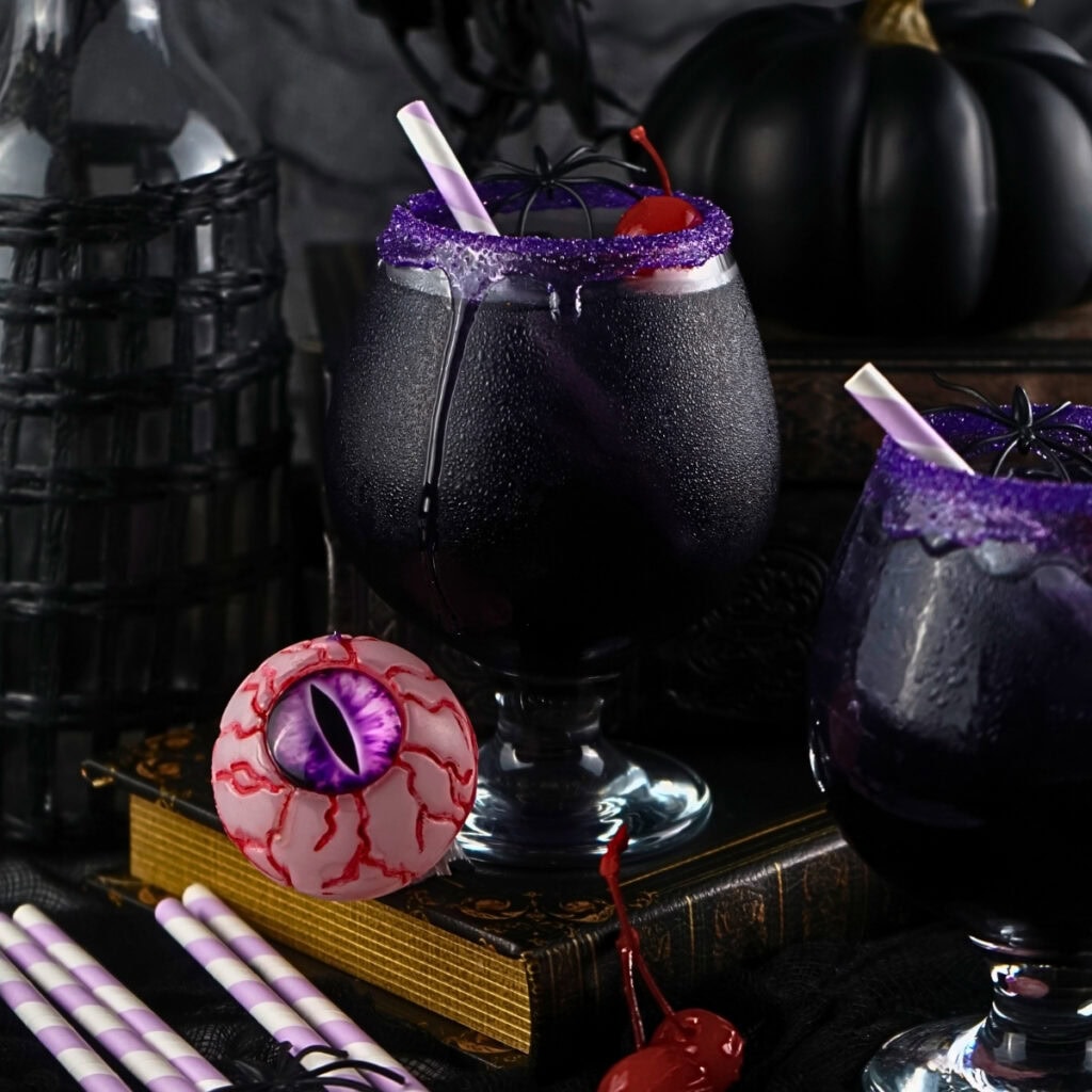 Black cocktail with purple sugar rim, cherry, and fake eyeball, Halloween decor.