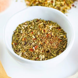 A white bowl filled with mixed dried herbs and spices on a white surface.