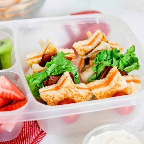 Star-shaped sandwiches with lettuce in a lunchbox, with fruit on the side.