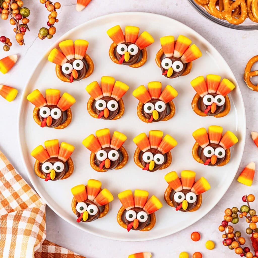 Candy turkeys with pretzels and candy corn are arranged on a white plate.