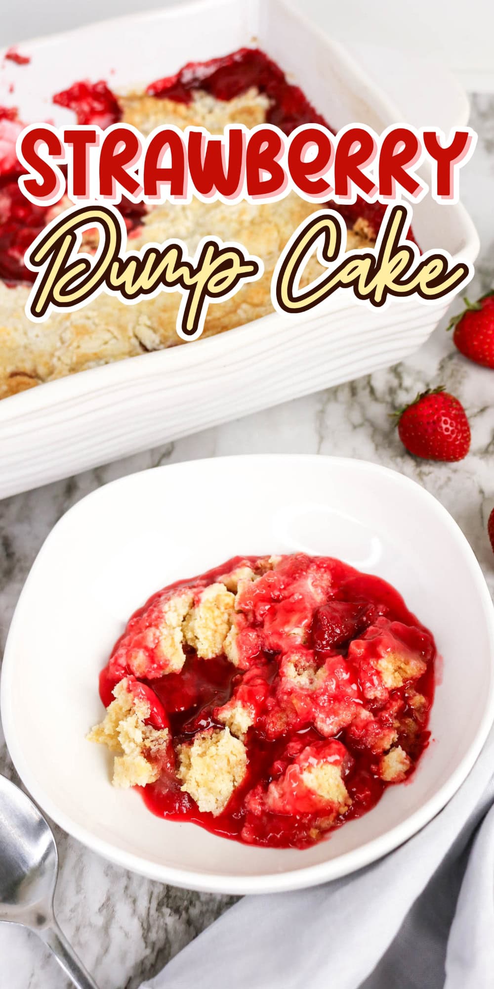 Bowl of strawberry dump cake with baking dish and fresh strawberries nearby.