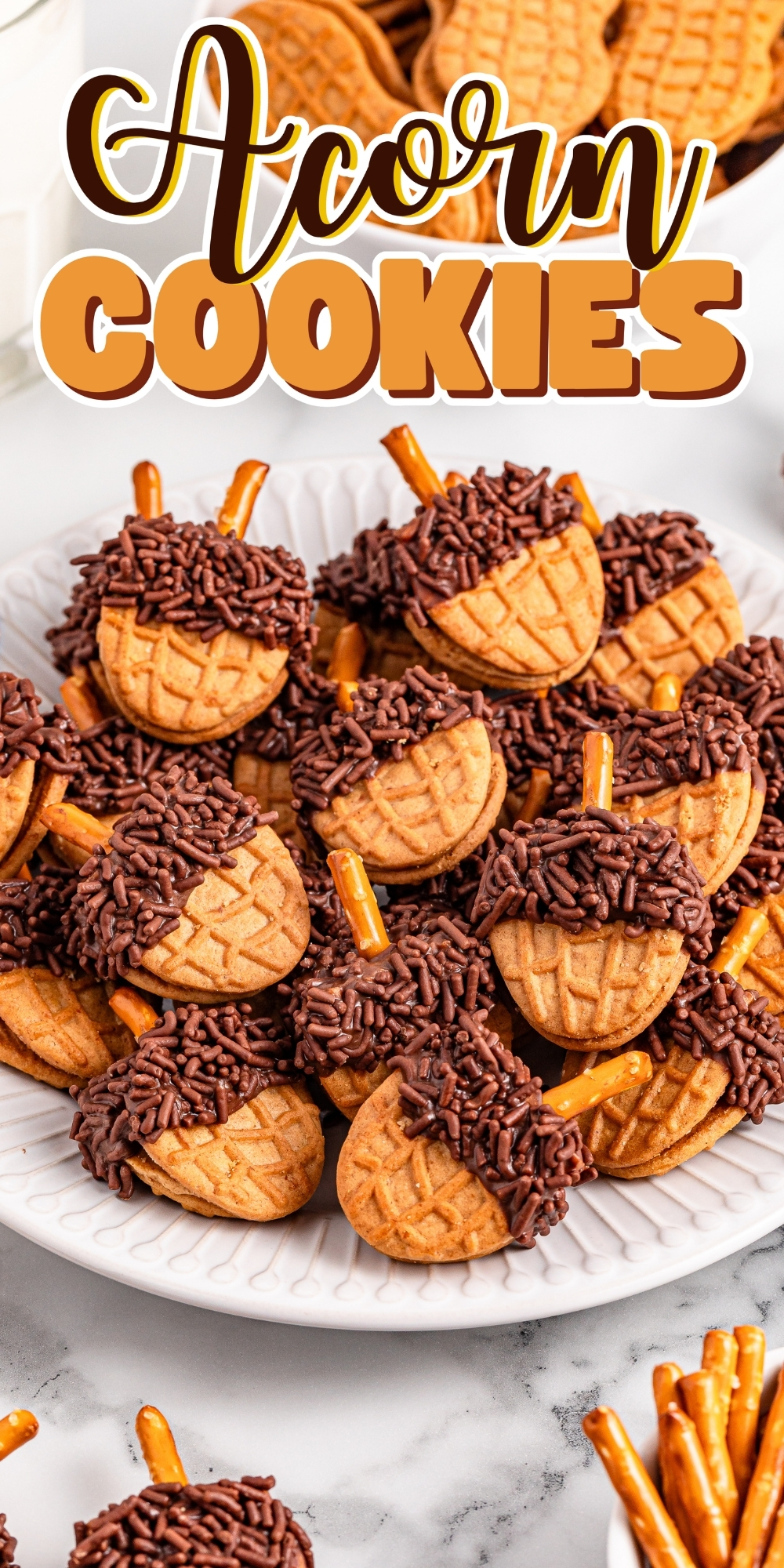 A plate of acorn-shaped cookies with chocolate and pretzel stick stems.